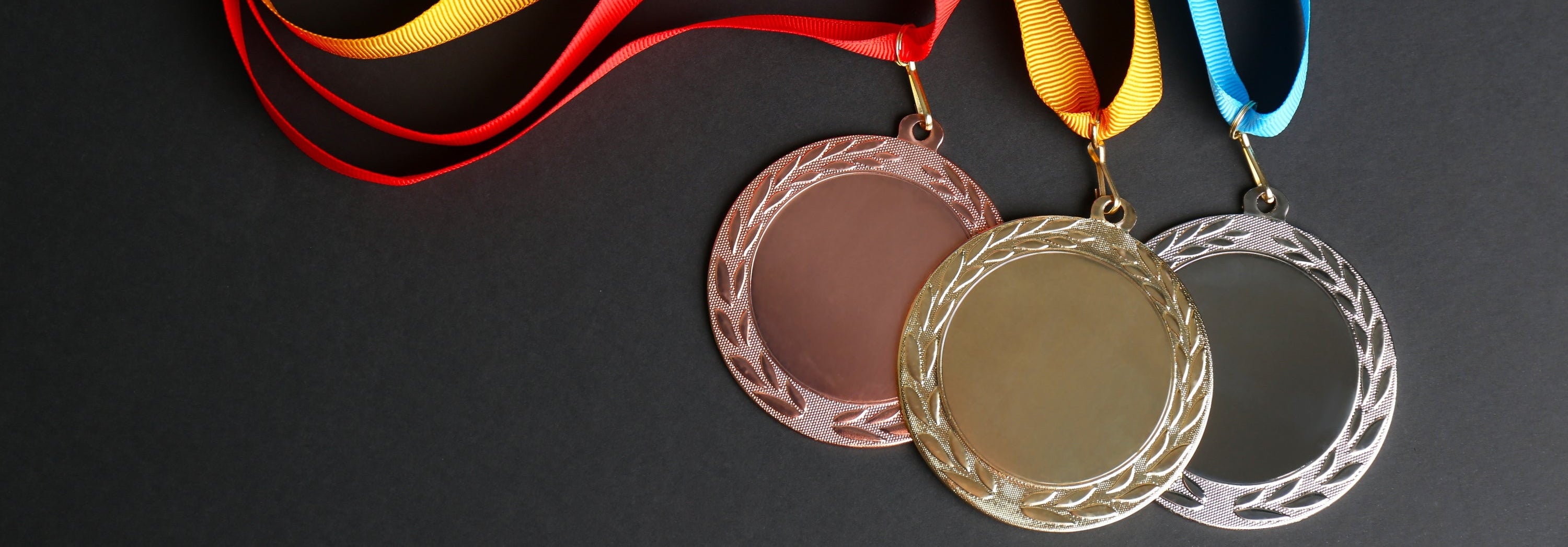 Gold, silver, and bronze medals with colorful ribbons on a dark background